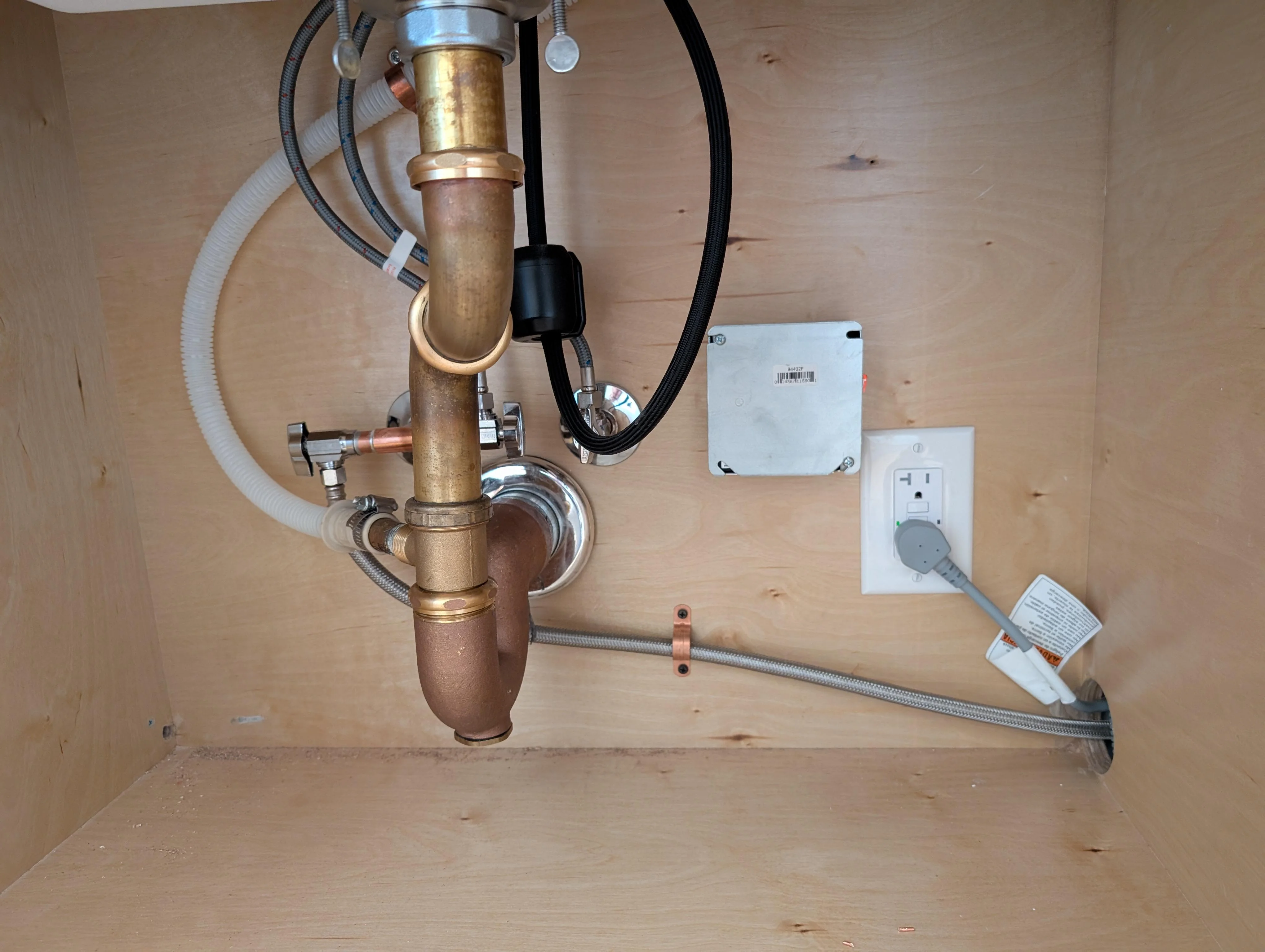 A GFCI electrical outlet mounted on the back wall inside a kitchen sink cabinet with a garbage disposal plug nearby