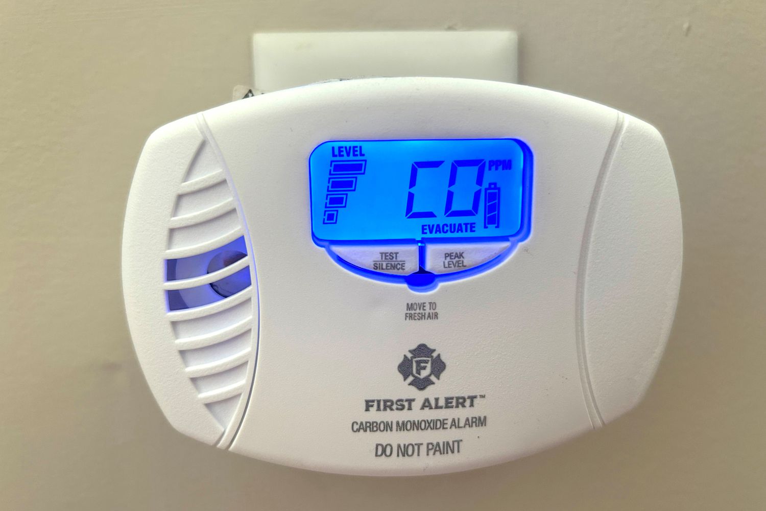 A carbon monoxide detector mounted in a hallway outside bedroom doors with natural indoor lighting