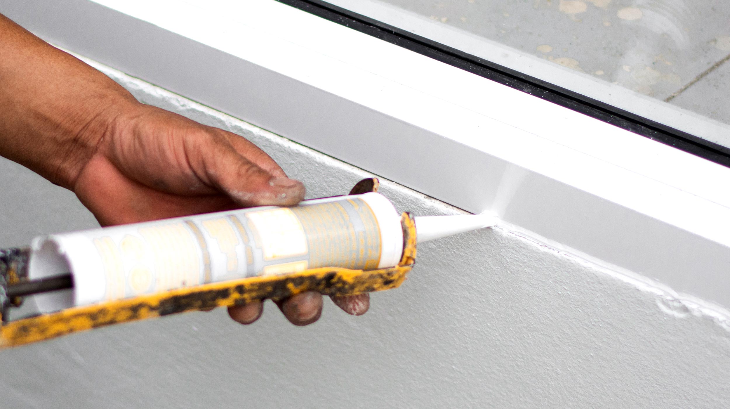 A caulk gun applying a neat bead of exterior caulk along the joint where window trim meets siding
