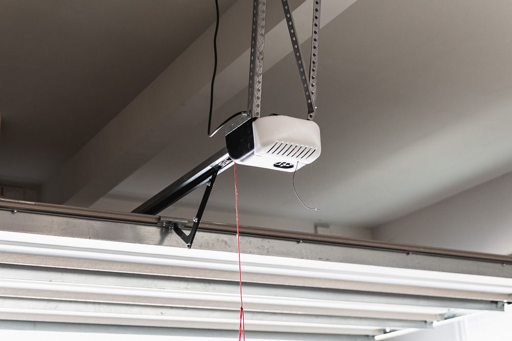 A ceiling mounted garage door opener with the cover removed slightly, showing the light lens and housing in a residential garage