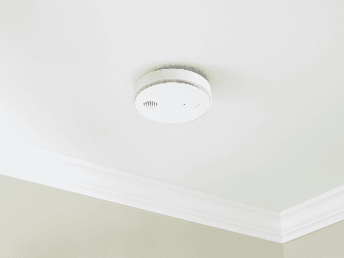 A ceiling-mounted residential smoke alarm installed on a white ceiling near a hallway, photographed in a real home