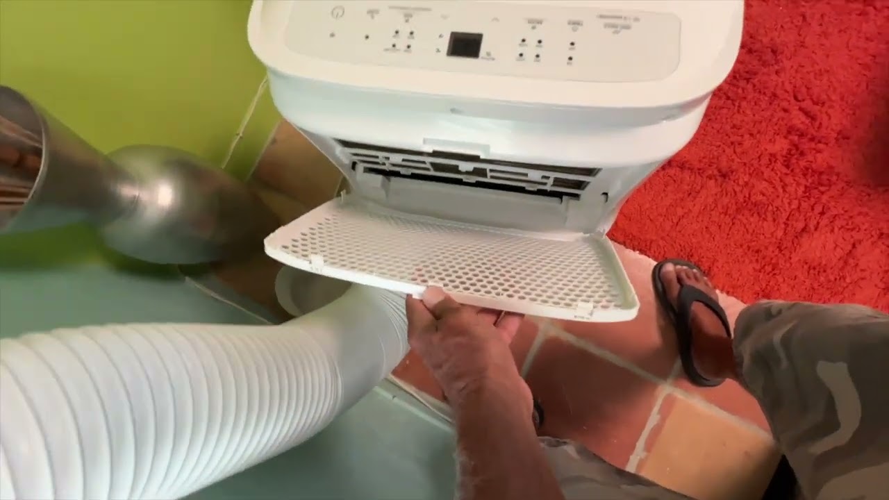 A close-up of a portable air conditioner rear panel with the air filter partially slid out, showing dust buildup on the mesh