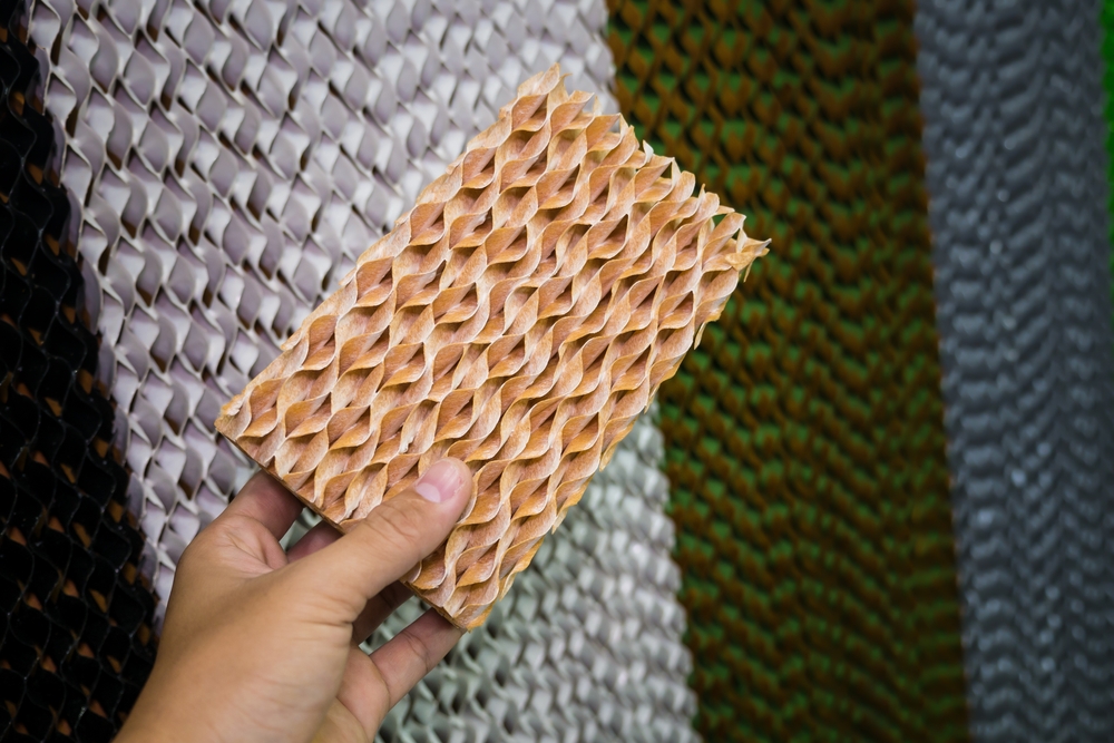 A close-up of a worn evaporative cooler pad with mineral crust and dry spots next to the cooler housing