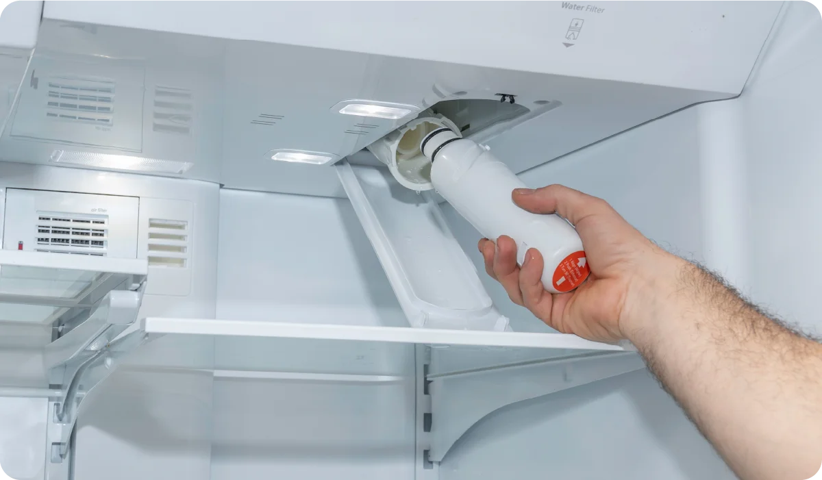 A close-up photo inside a refrigerator showing a water filter compartment with a round filter cartridge seated in a plastic housing