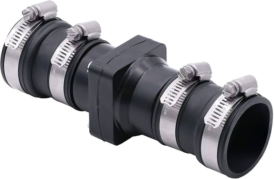 A close-up photo of a PVC sump pump discharge pipe with a rubber coupler check valve installed vertically, metal hose clamps visible in a basement