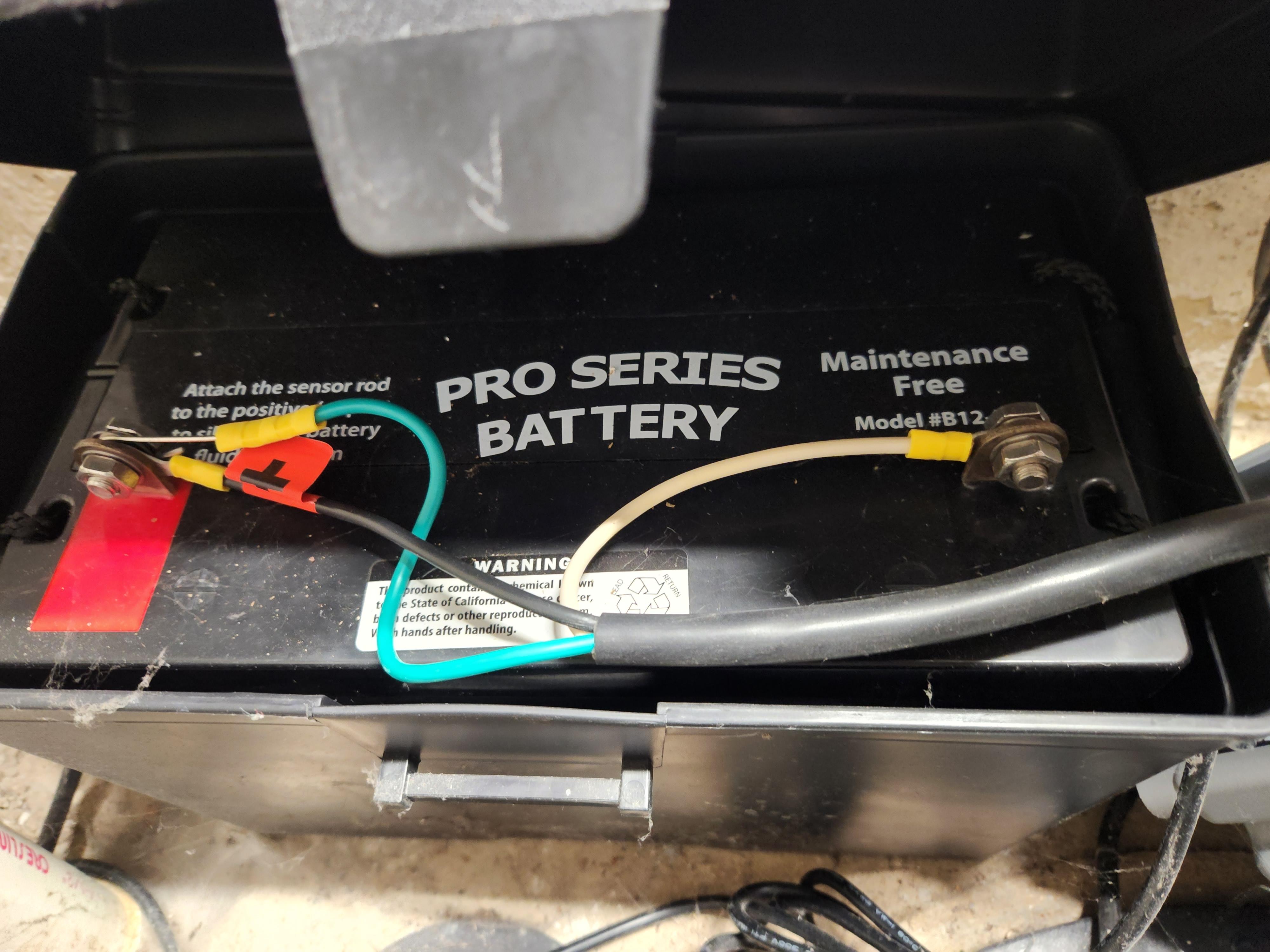 A close-up photo of a deep-cycle battery terminal with visible corrosion next to a sump pump backup cable end, realistic indoor lighting