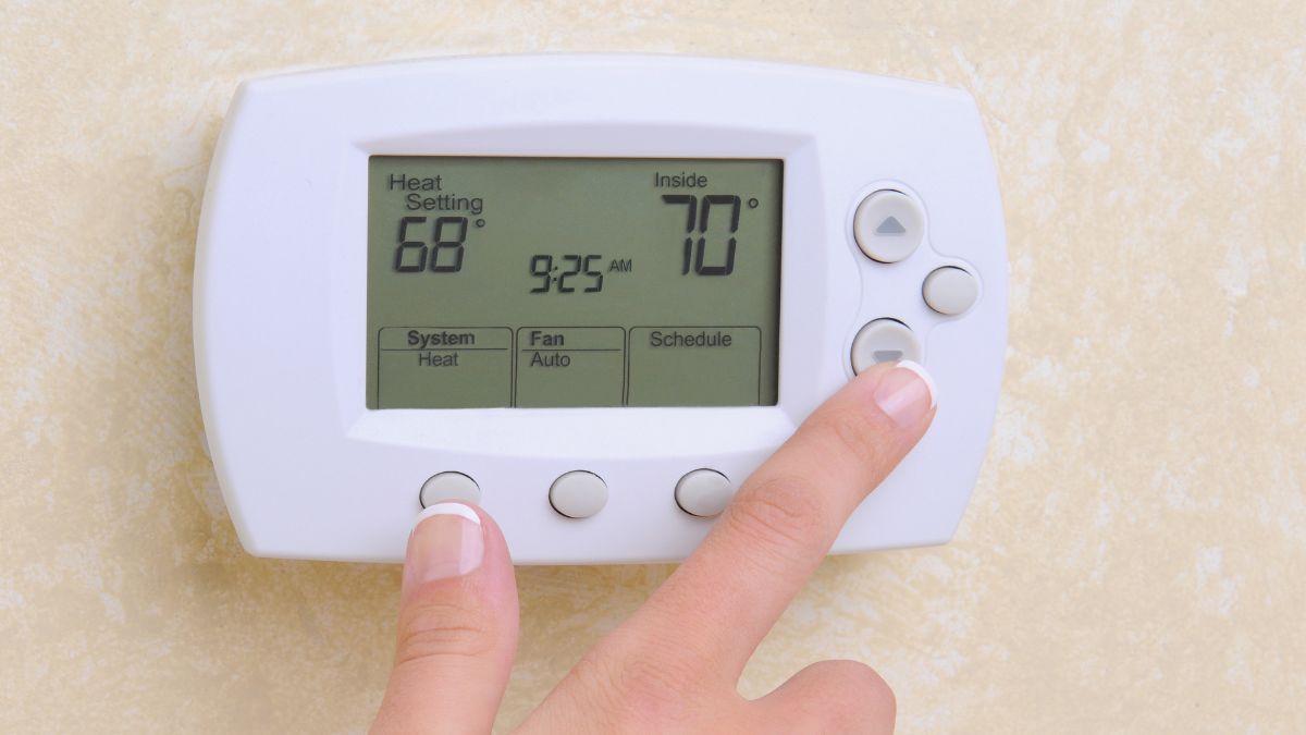 A close-up photo of a digital thermostat on a wall set to cooling mode with a summer temperature setpoint, real photography