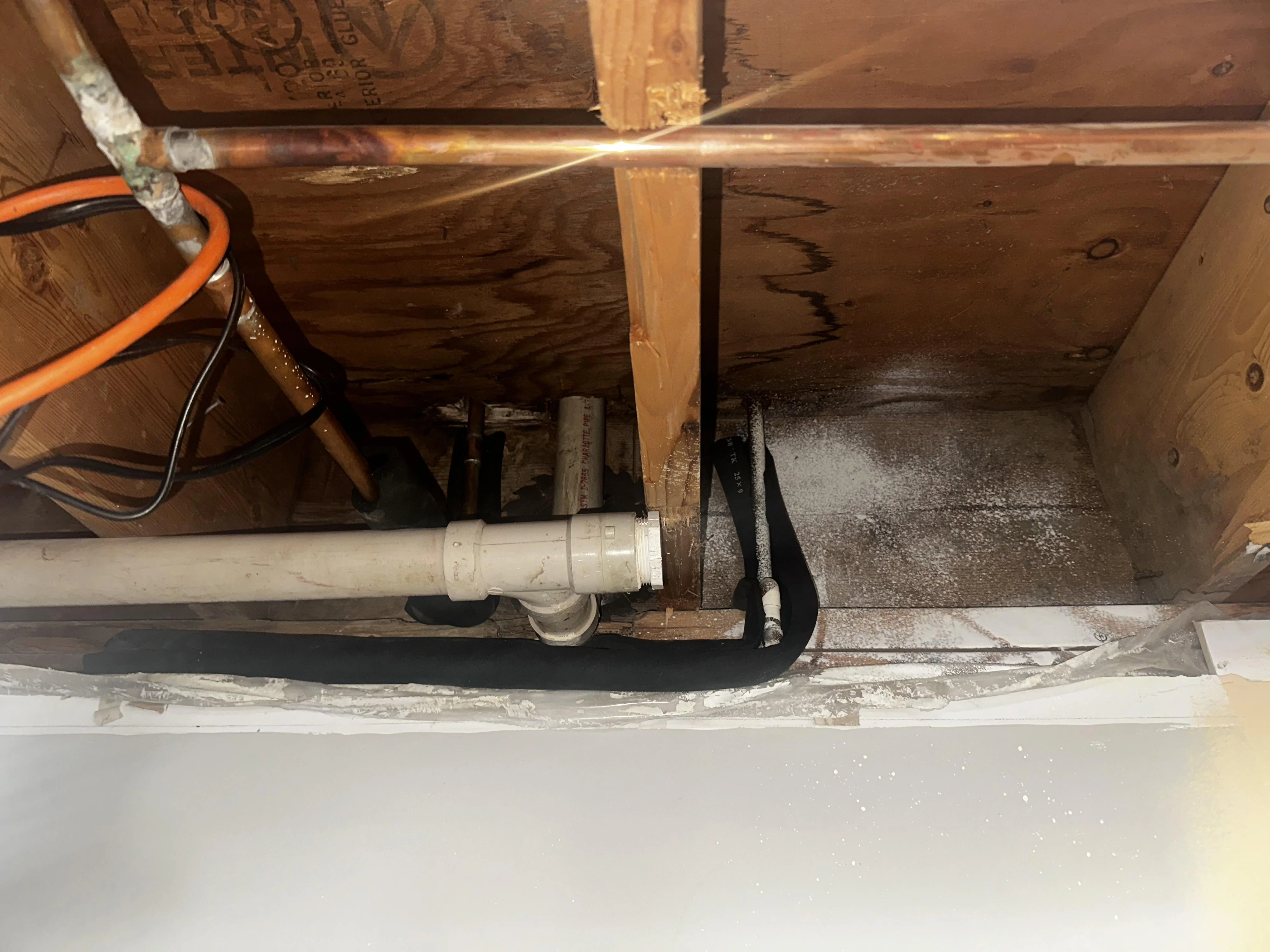 A close-up photo of a frozen copper water pipe under a kitchen sink with visible frost and a slightly open cabinet door, realistic indoor lighting