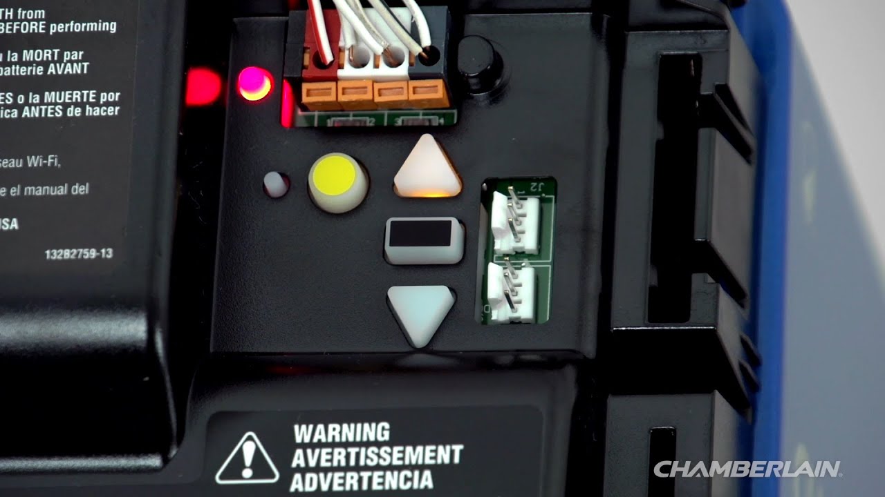 A close up photo of a garage door opener motor unit showing the learn button and indicator LED near the light lens