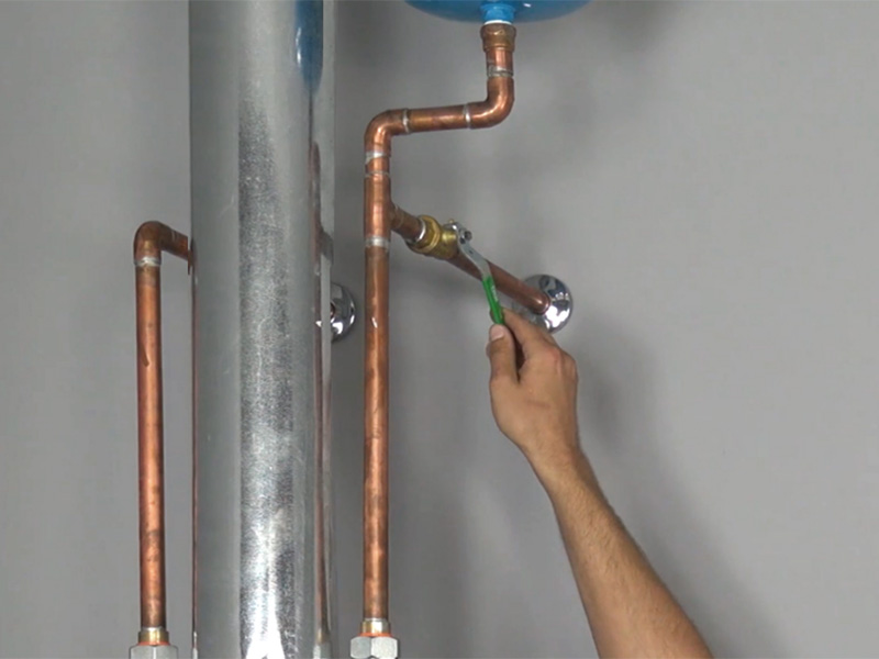 A close-up photo of a homeowner hand turning the cold water shutoff ball valve above a basement water heater
