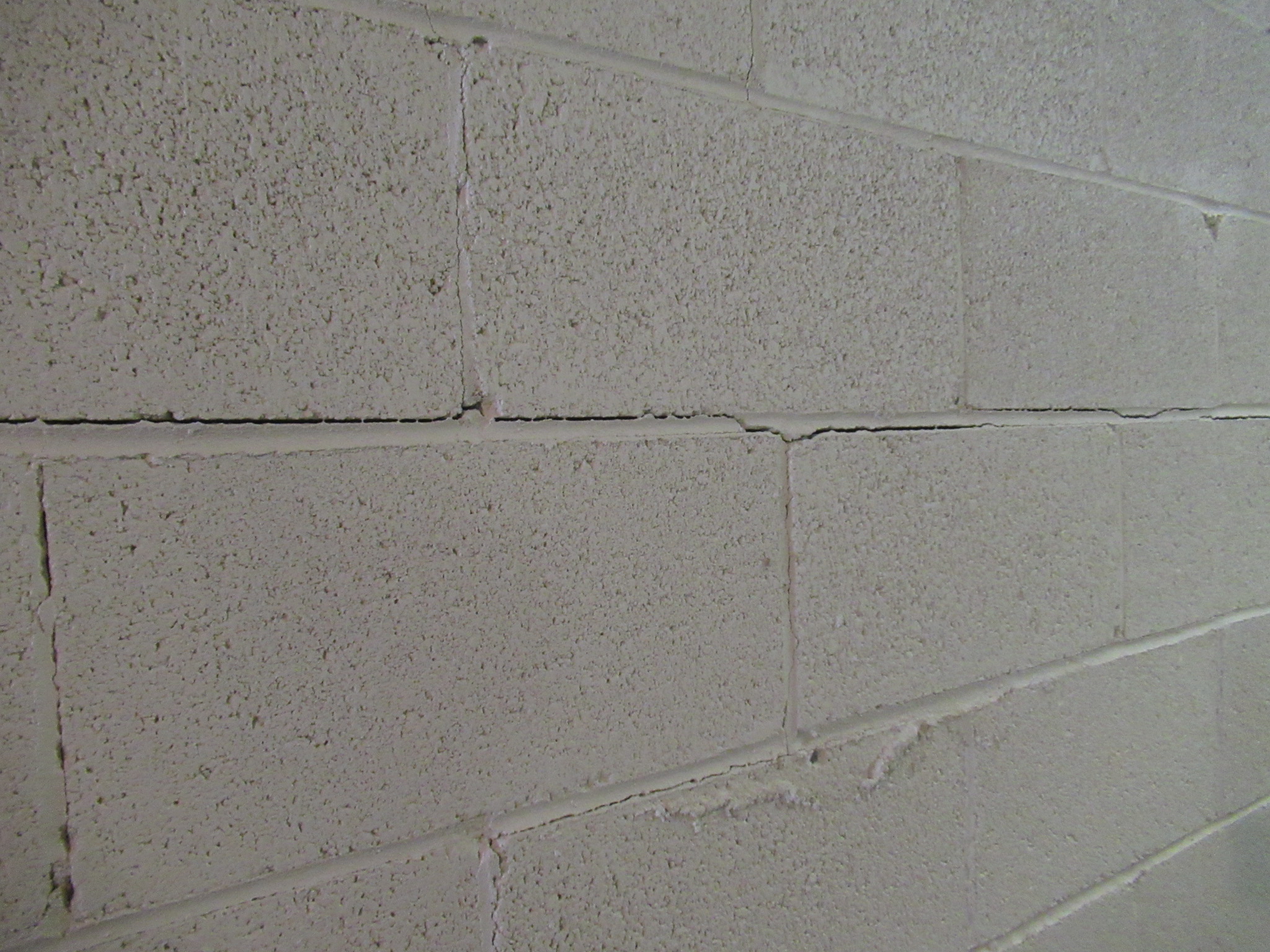 A close-up photo of a horizontal crack running through concrete block courses on a basement wall, with mortar lines visible and slight inward displacement