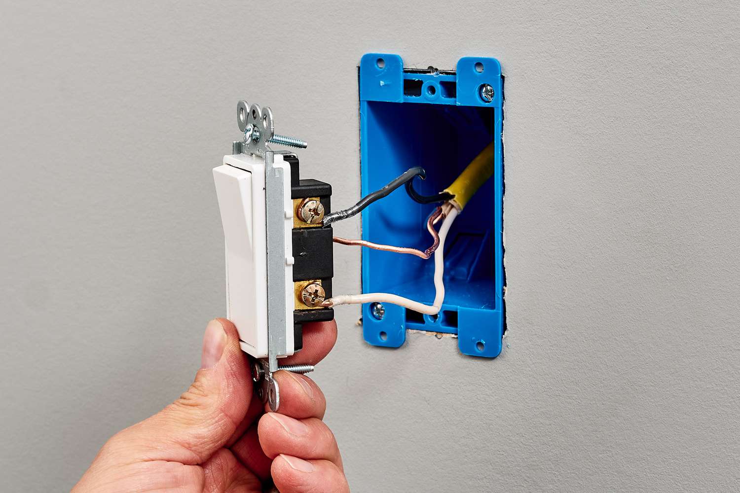 A close-up photo of a light switch pulled out from the wall showing the wires connected to the side screws