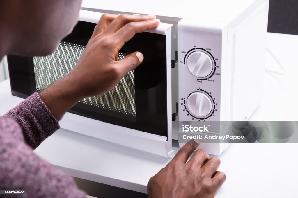 A close-up photo of a person pressing the door-open button on a countertop microwave in a home kitchen