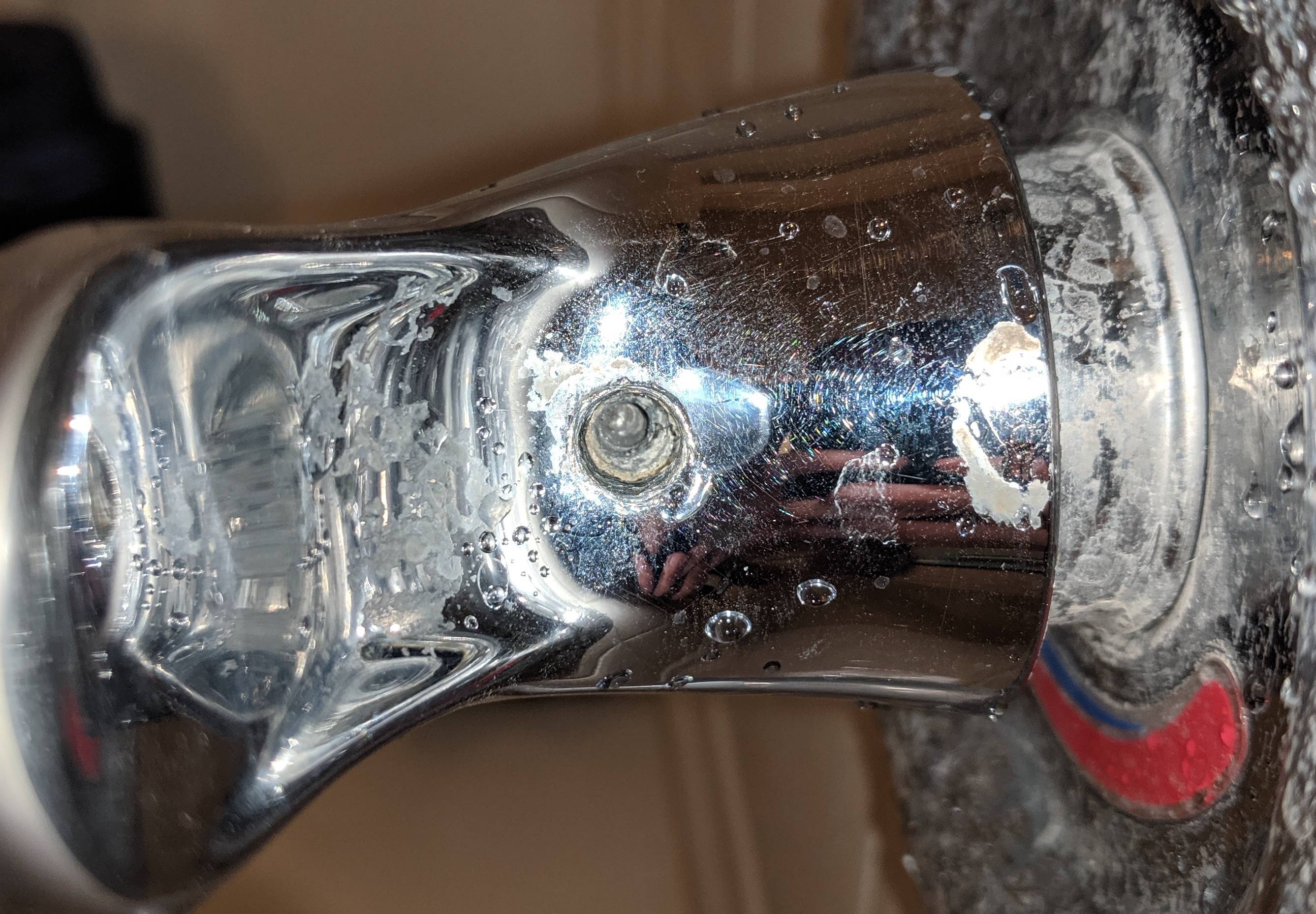 A close-up photo of a person using an Allen key to loosen the set screw on a shower handle, bathroom lighting