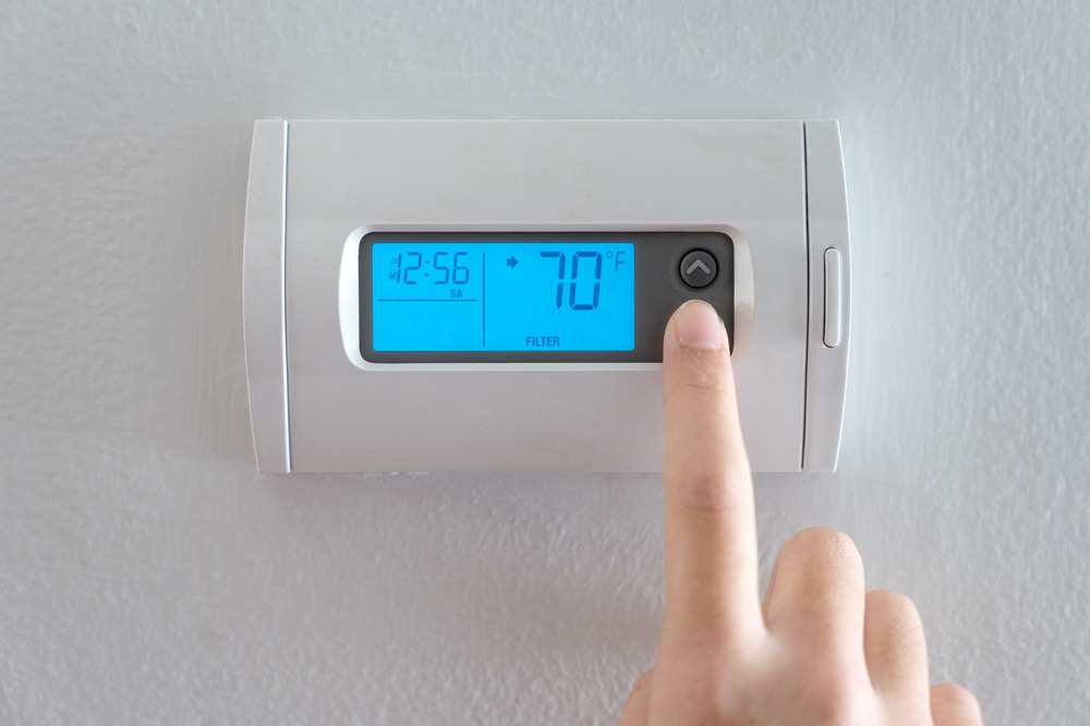 A close-up photo of a person’s hand adjusting a home thermostat while listening for the AC to start