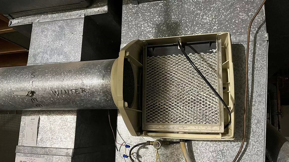A close-up photo of a round bypass duct connected between furnace supply and return ducts on a bypass humidifier, showing sheet metal screws and foil tape