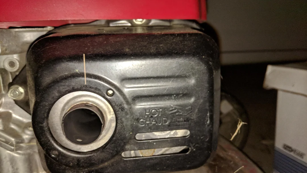 A close-up photo of a small lawn mower engine with light smoke drifting from the muffler area outdoors