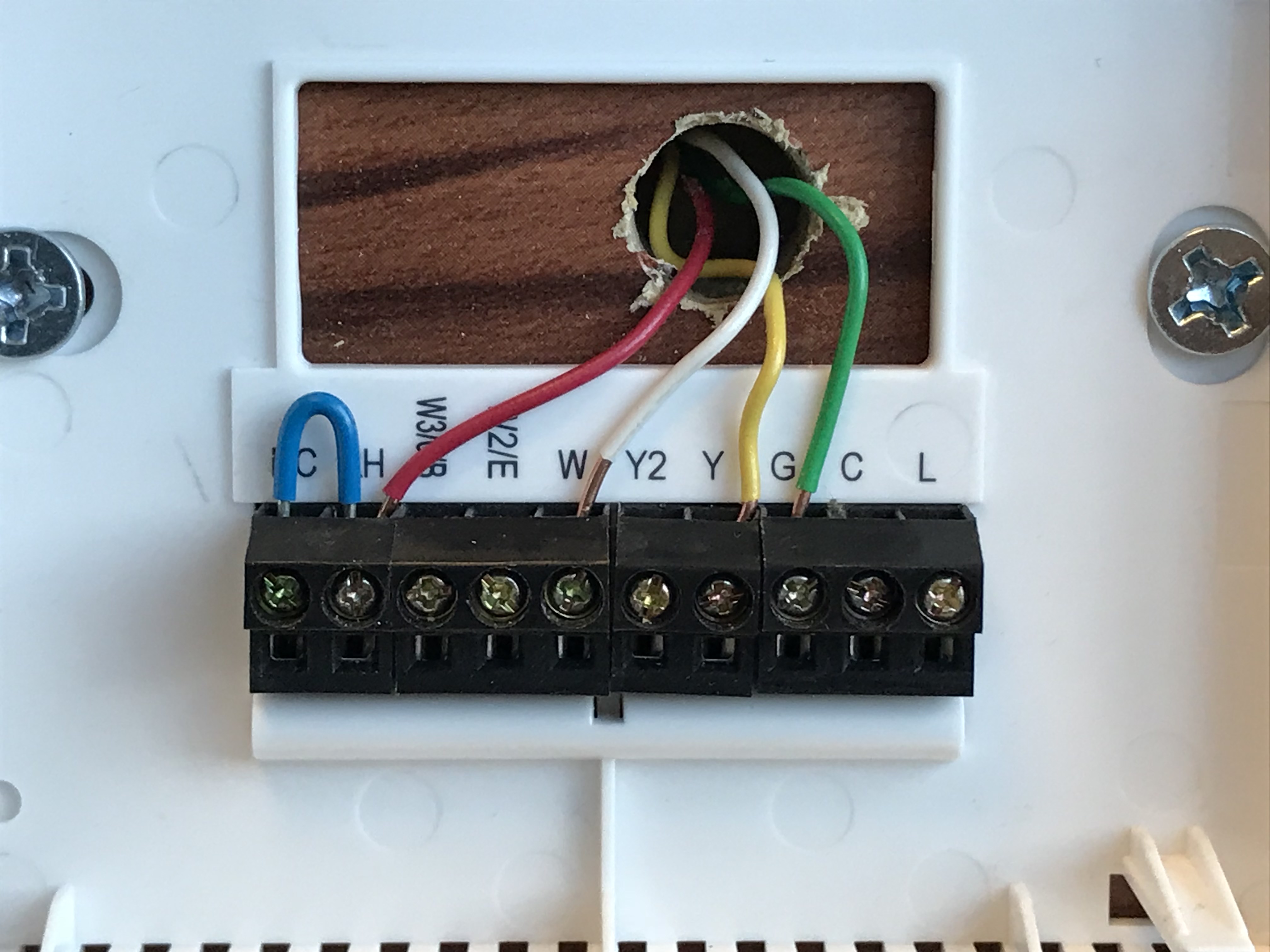 A close-up photo of a smart thermostat wall plate with labeled terminals and several colored wires connected, including a wire at the C terminal