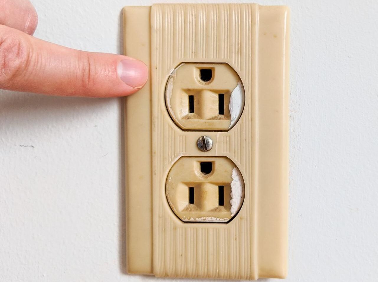 A close-up photo of a standard kitchen wall outlet with slight discoloration around the slots and a microwave plug that sits loosely, shallow depth of field