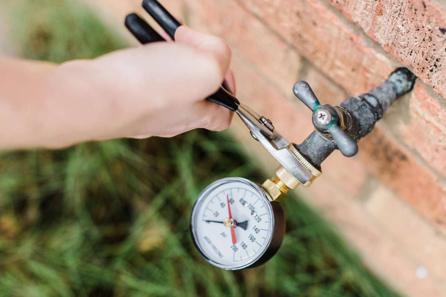 A close-up photo of a water pressure gauge attached to an outdoor hose bib on a house, showing a needle reading near the high end of the scale