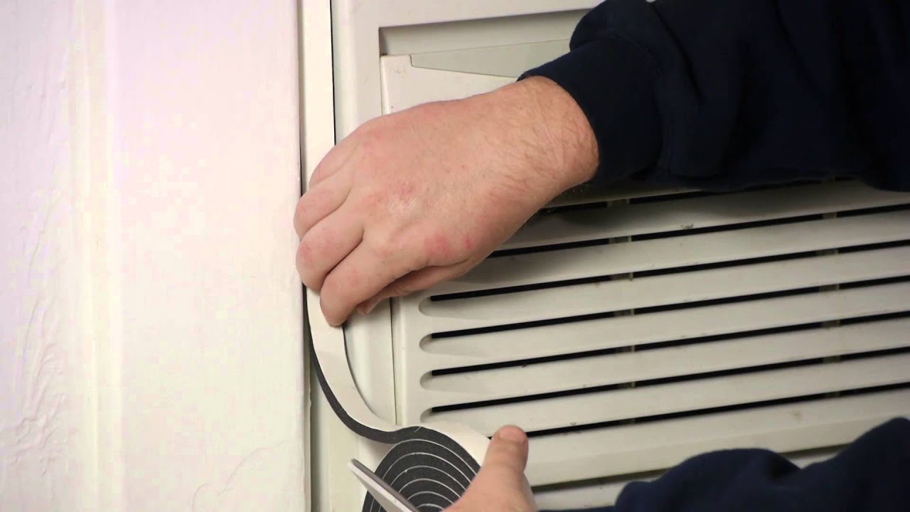 A close-up photo of a window air conditioner side accordion panel with a strip of gray foam weatherstripping being pressed into the gap between the panel and the window frame