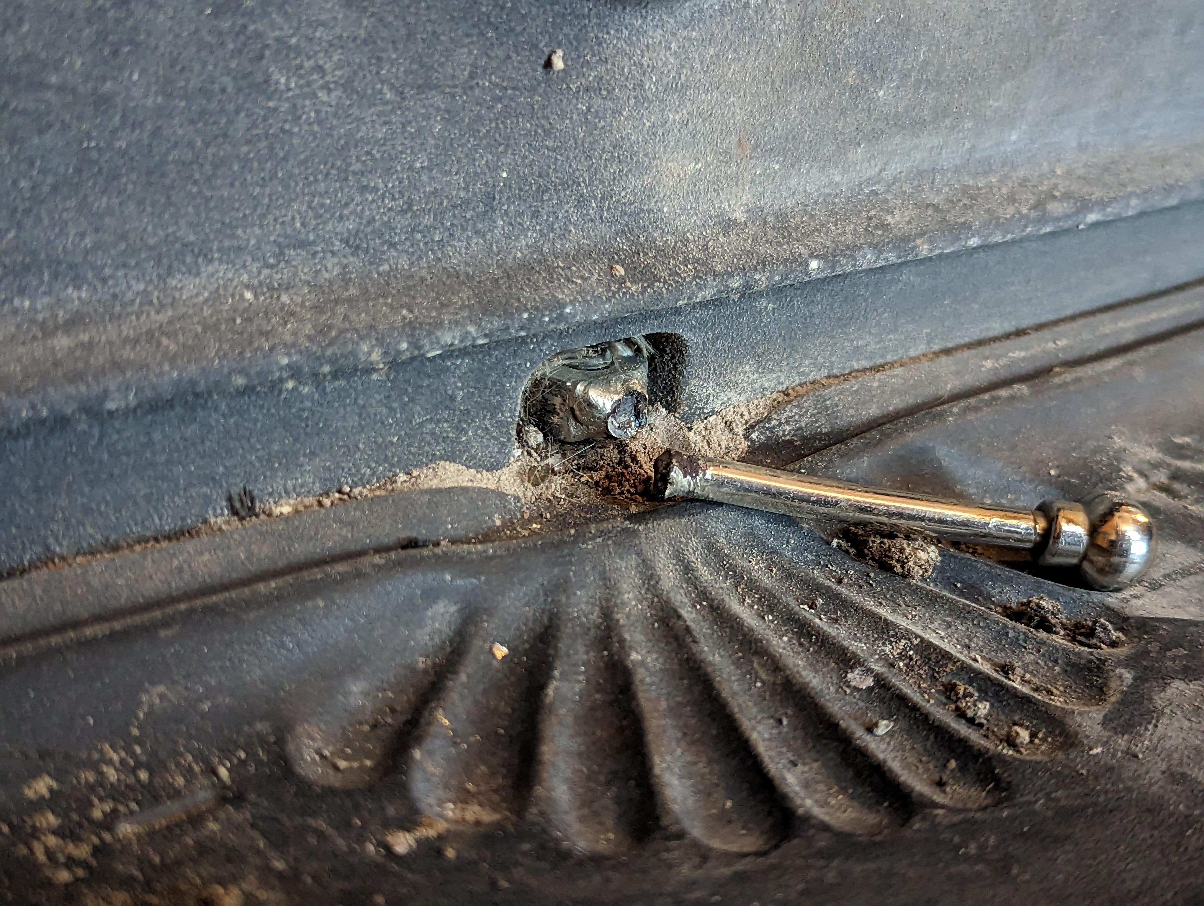 A close-up photo of a wood stove air control lever on the front of a black cast iron stove, indoor workshop lighting