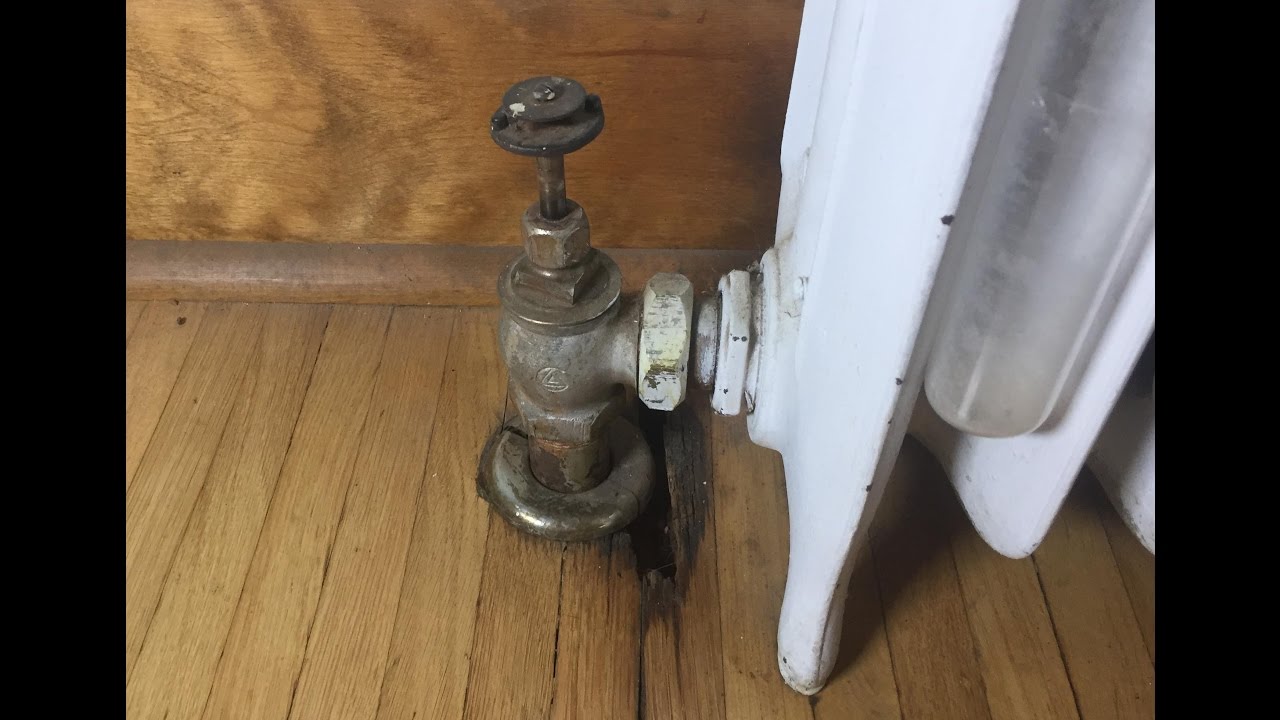 A close up photo of an old cast iron radiator shutoff valve with a round metal handle and aged brass body, typical of steam heat systems