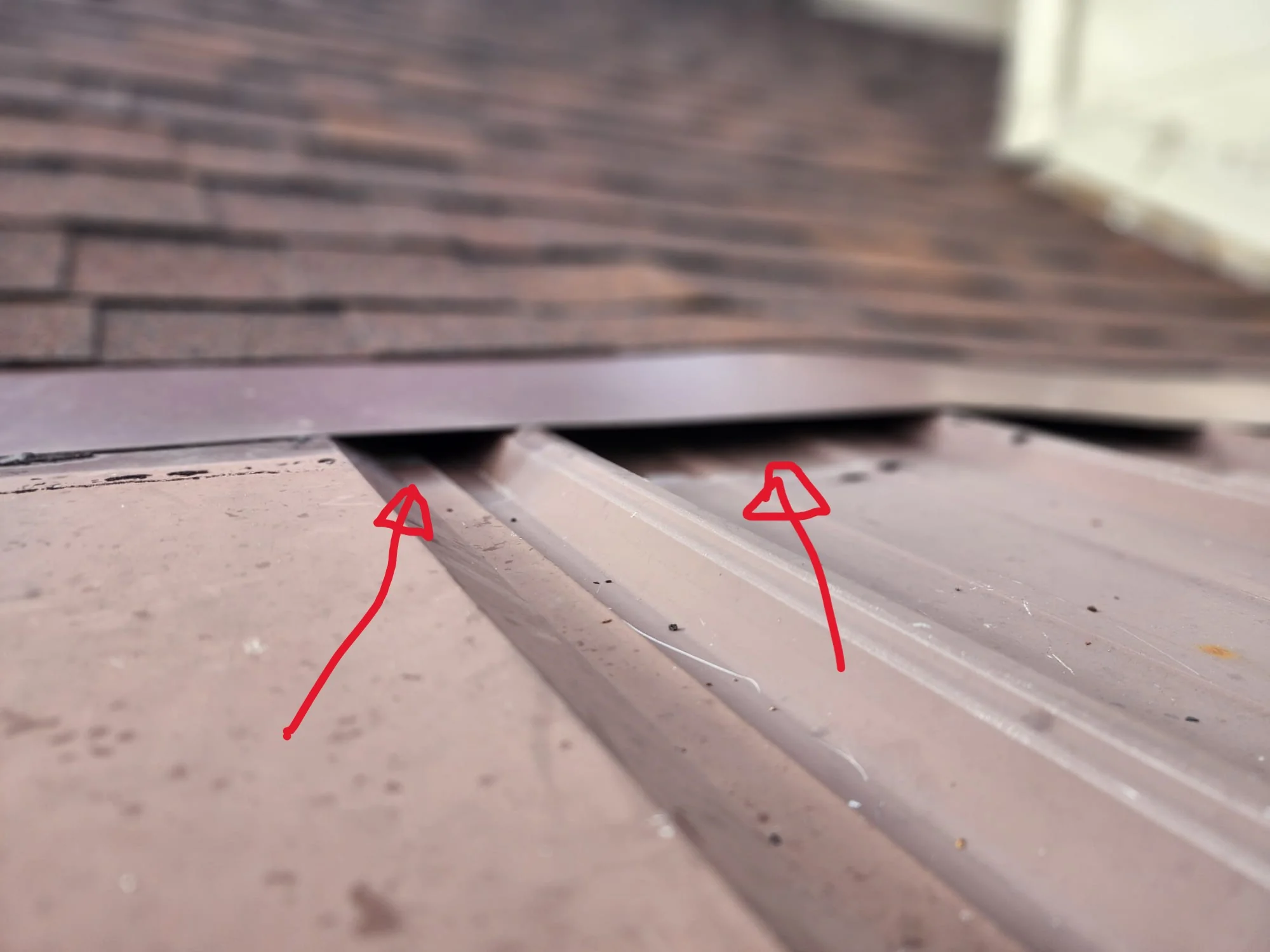 A close-up photo of hands installing metal flashing and applying exterior sealant to close a roofline gap near fascia boards