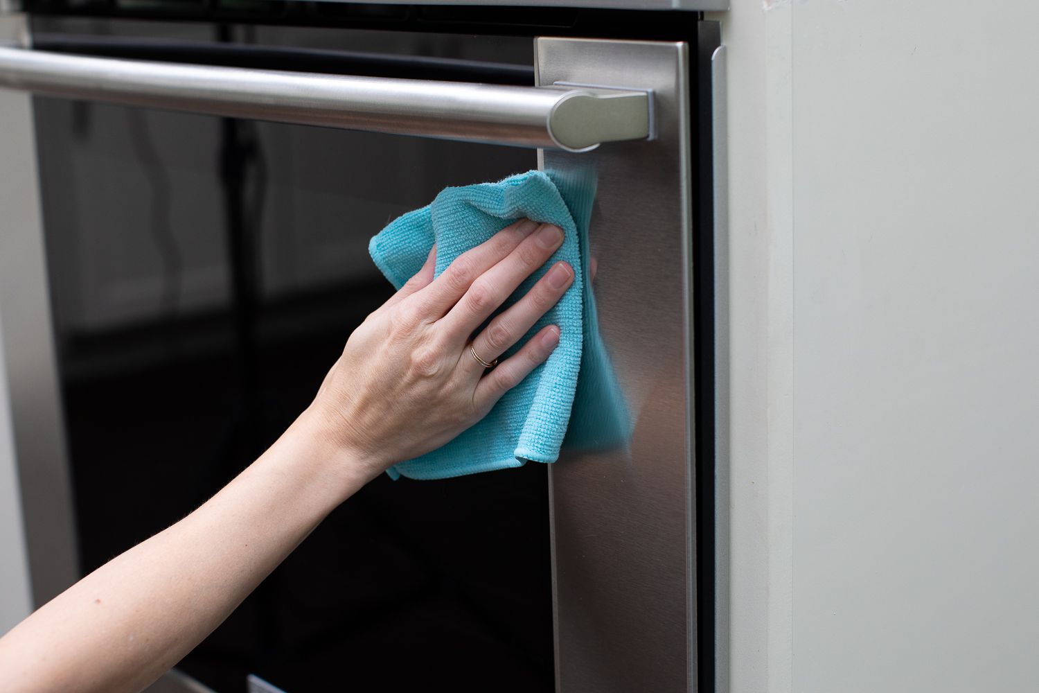 A close up photo of hands wiping the bottom edge of an oven door with a damp microfiber towel and mild cleaner