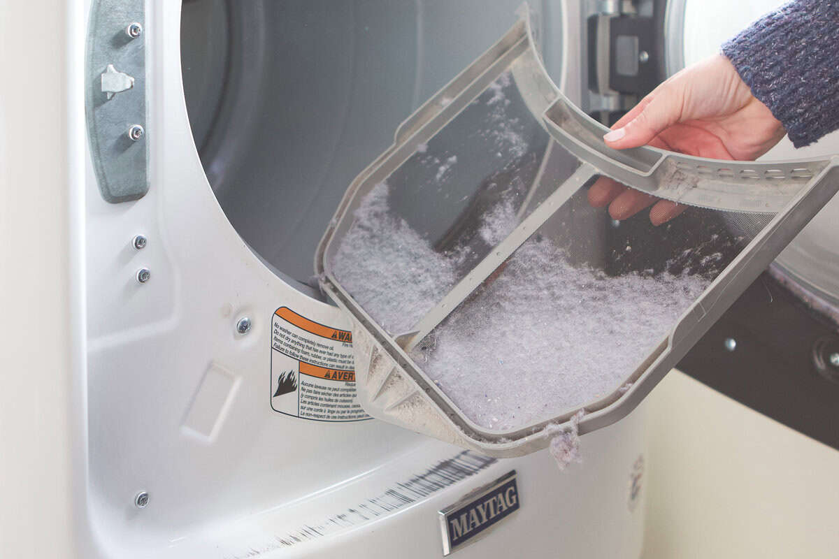 A close-up photo of lint buildup packed inside a dryer lint chute area with the lint screen removed, real photo style