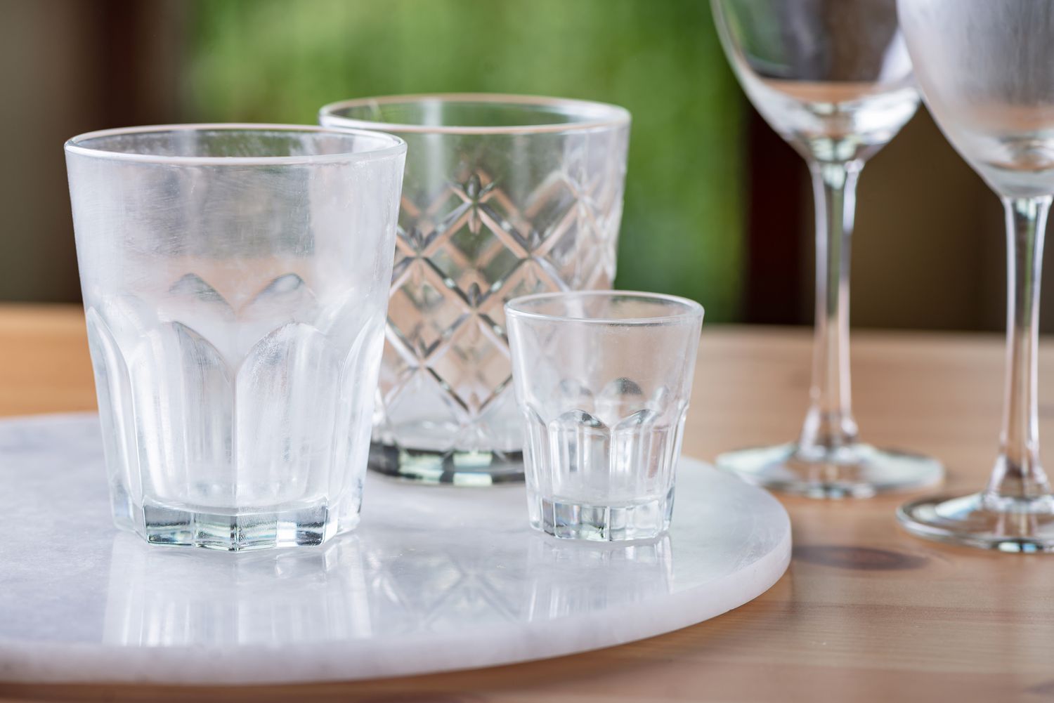 A close-up photo of several drinking glasses on a kitchen counter showing a cloudy white film after being run through a dishwasher, natural window light, realistic home setting
