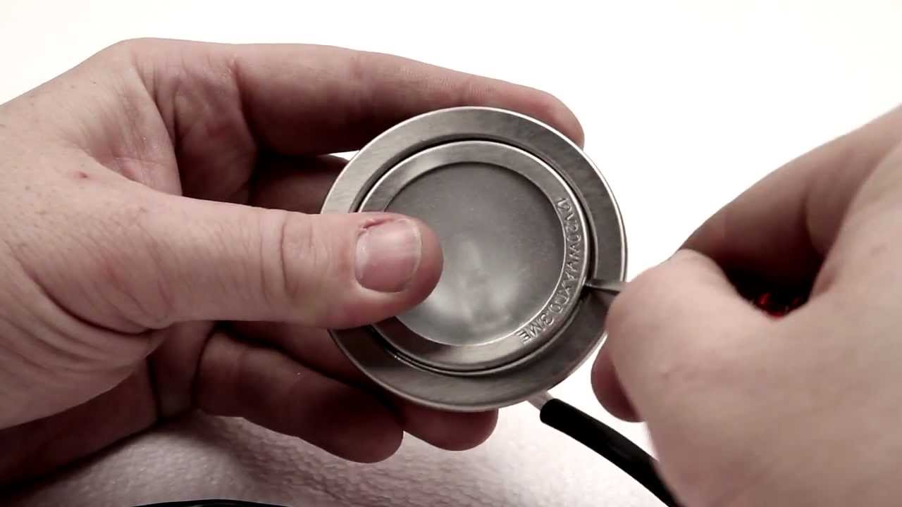 A close-up photograph of a small halogen range hood bulb removed from its socket, showing the metal base and voltage markings