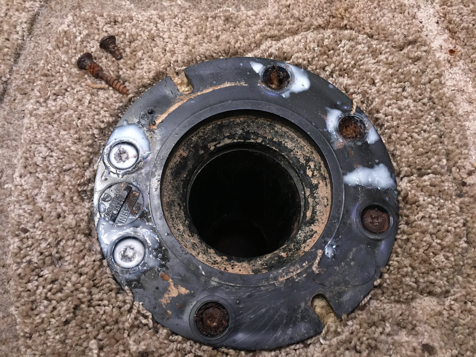 A close-up photograph of a toilet flange with a broken closet bolt slot and old wax scraped away