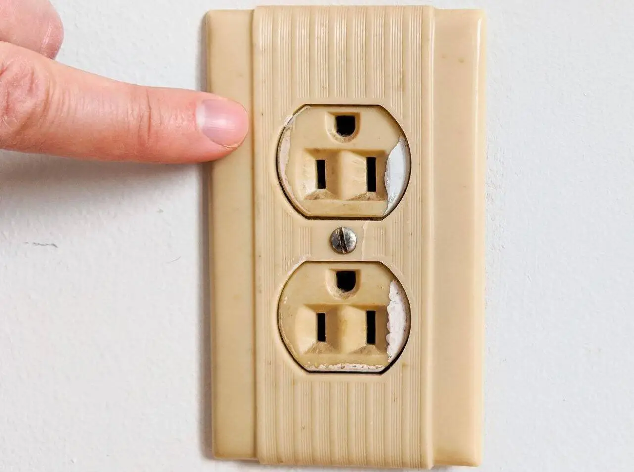A close-up photograph of an older duplex electrical outlet with visible discoloration around one slot