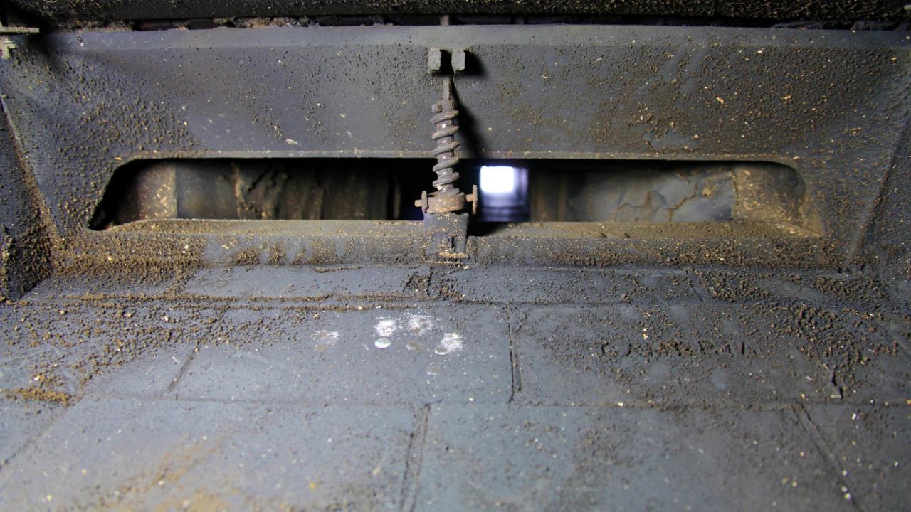 A close-up real photo of a masonry fireplace firebox showing the metal damper mechanism and soot-stained brick interior