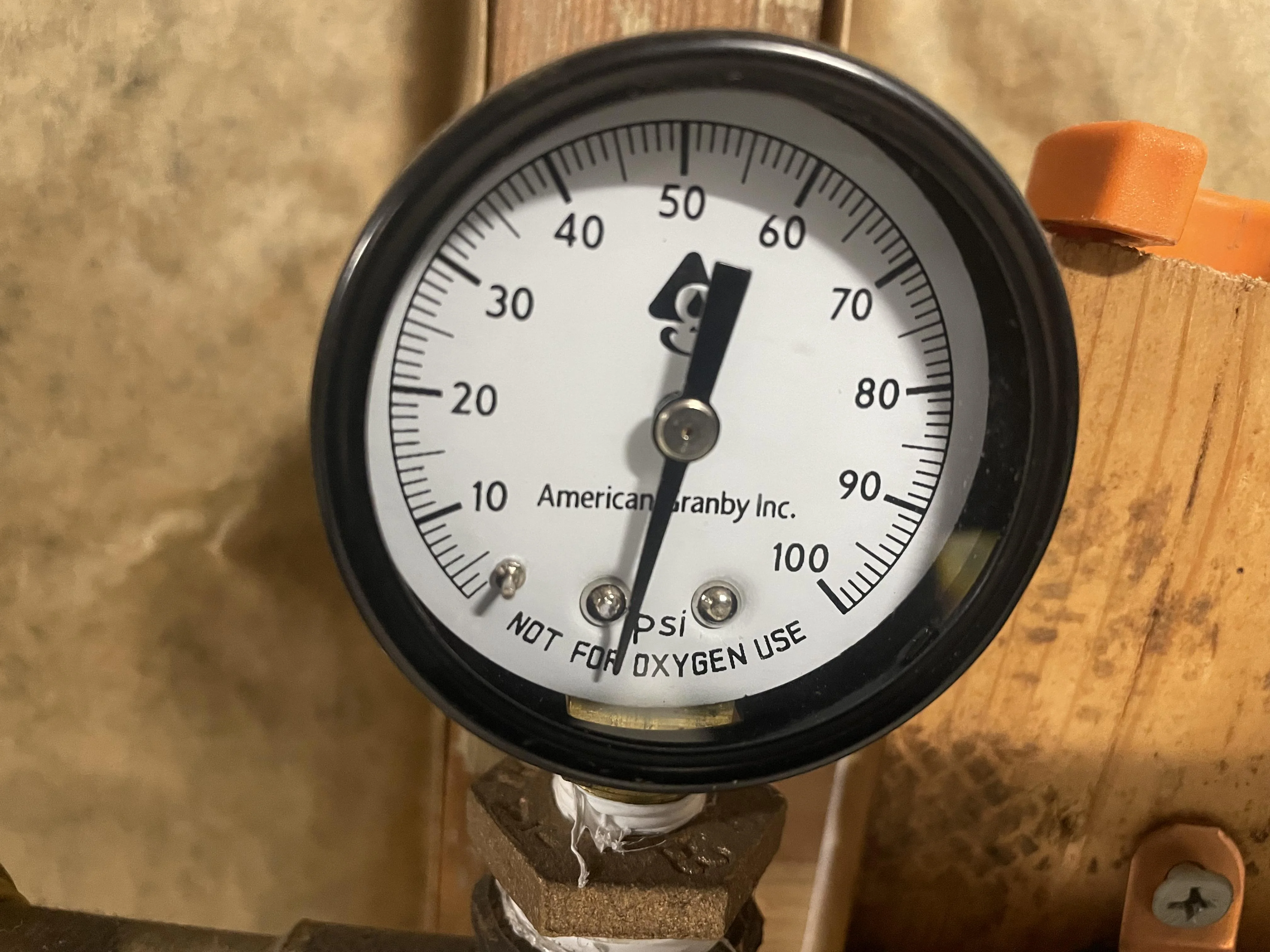 A close-up real photo of a water pressure gauge attached to an outdoor hose bib on a house, showing a high reading around 90 PSI in daylight