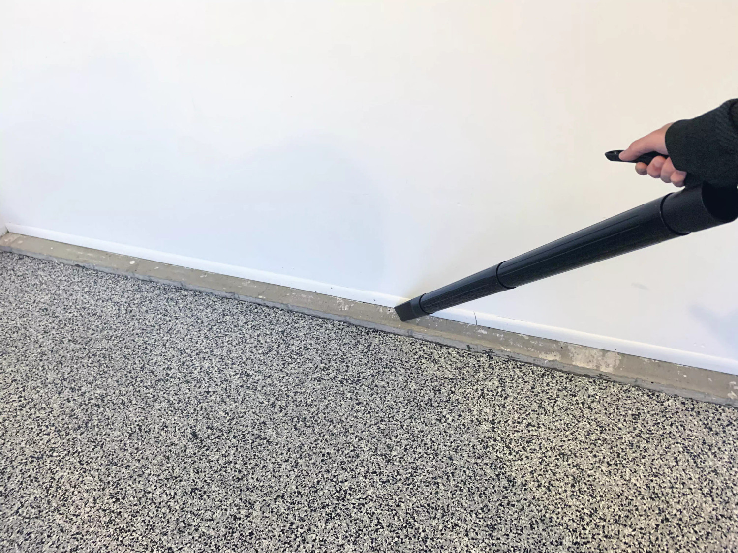 A close up view of a vacuum crevice tool cleaning along a dusty baseboard edge in a storage area