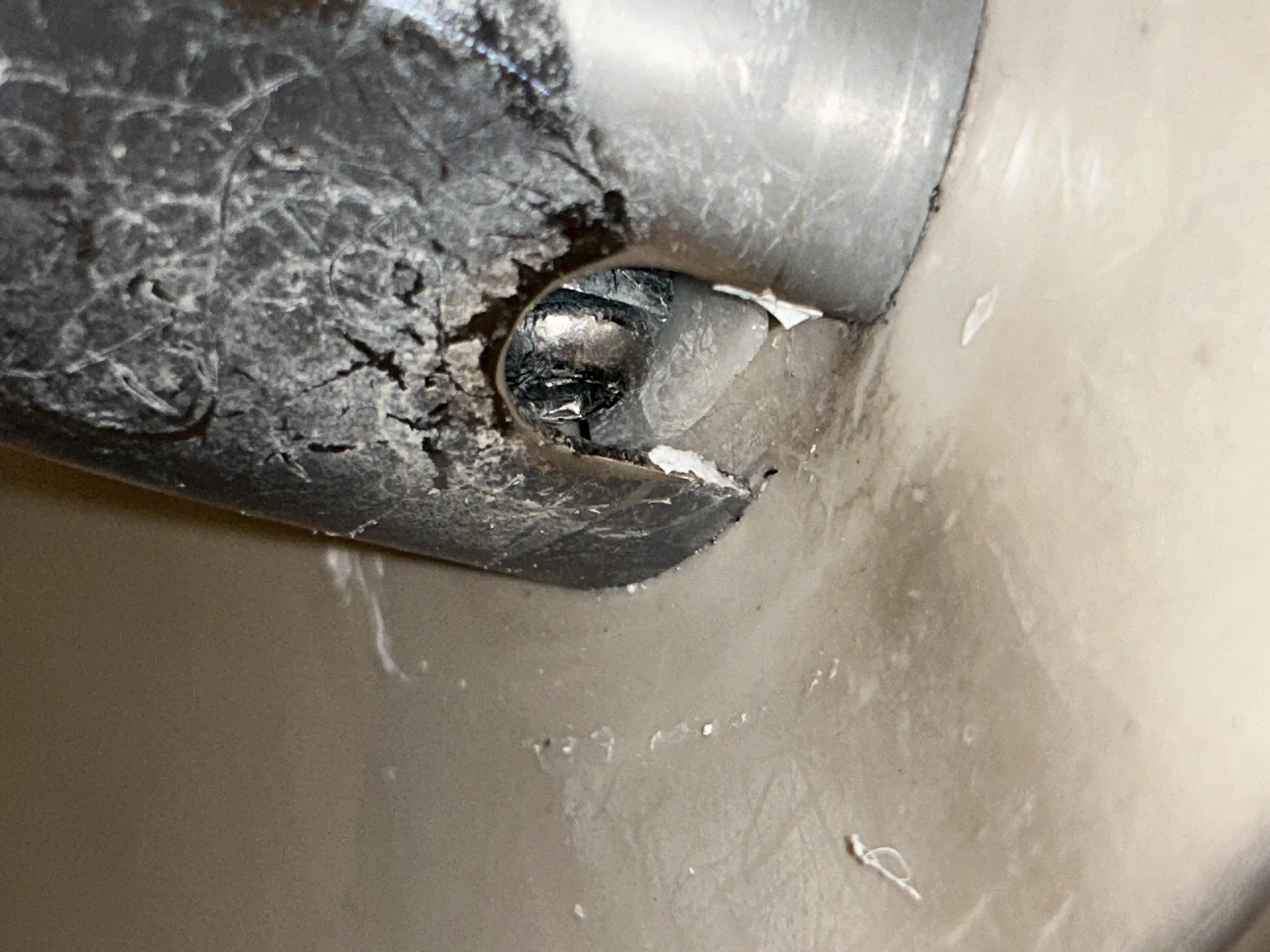 A close-up view of the underside of a bathtub spout showing the small set screw near the wall