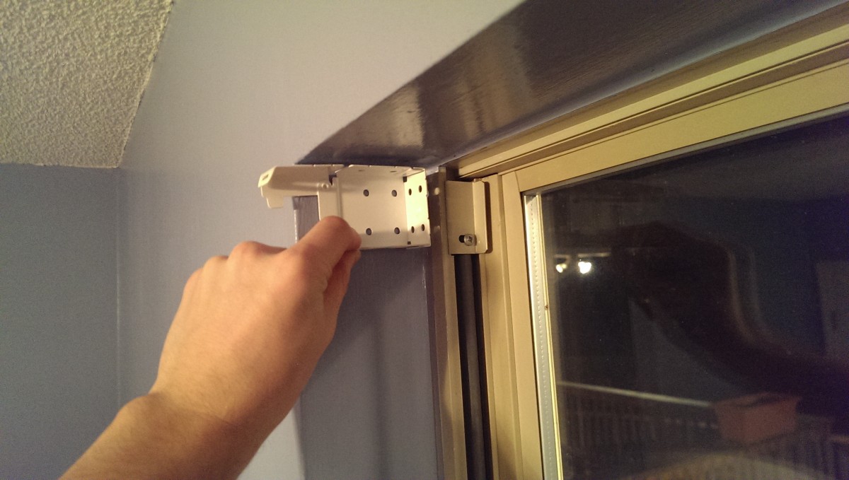A close view of a pencil marking screw hole locations for window blind brackets on painted wood trim