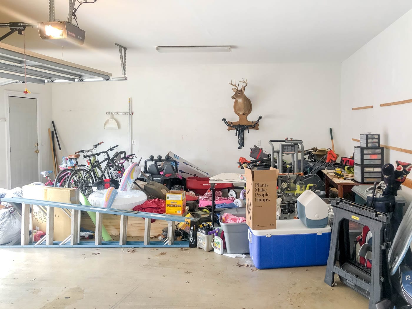A cluttered garage corner with stacked cardboard boxes, wood scraps, and tools stored against the wall, creating dark undisturbed gaps
