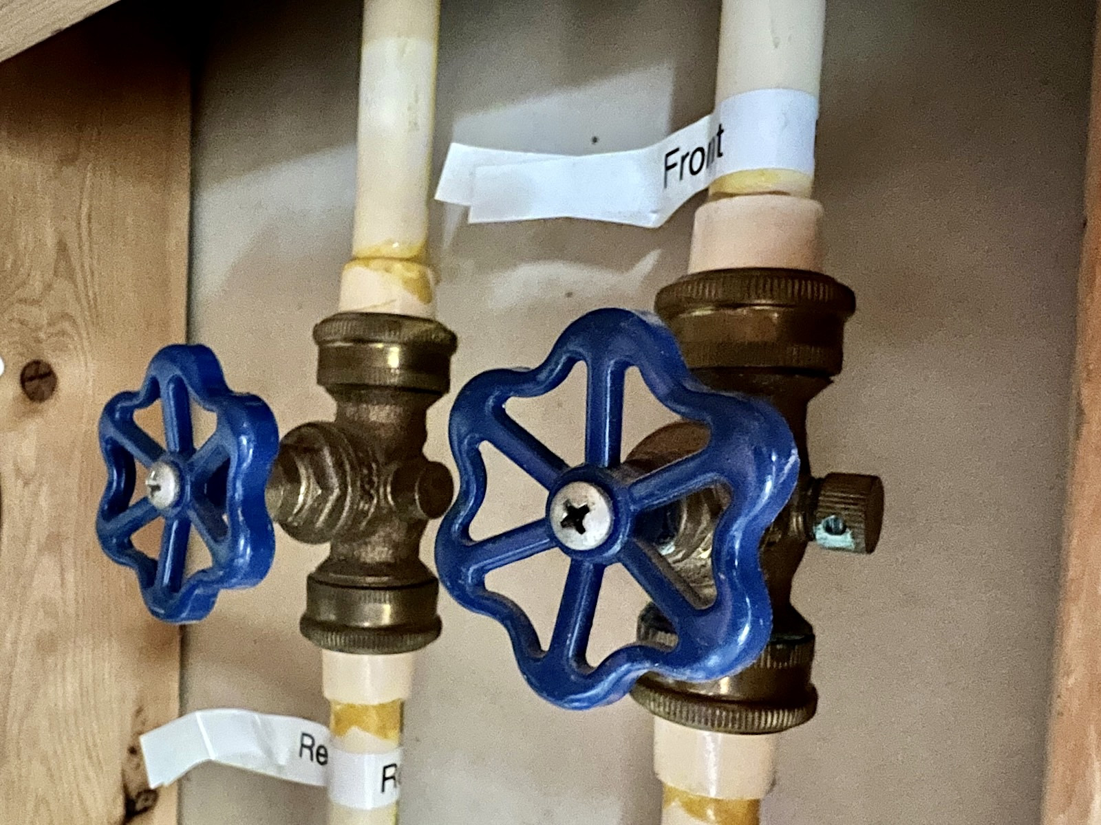 A copper water line in a basement with a small quarter-turn ball valve labeled by location, photographed close up with tools nearby