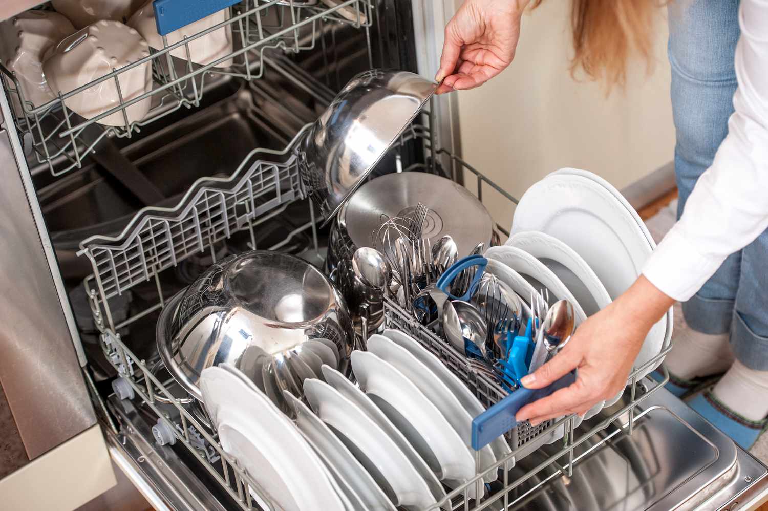A dishwasher bottom rack loaded with plates facing inward and a few pots placed along the sides, leaving space for water spray