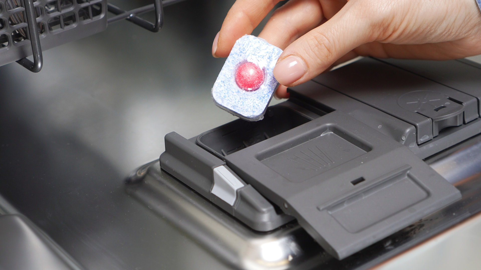 A dishwasher detergent pod sitting inside the main detergent dispenser cup on the door, with the dispenser lid open