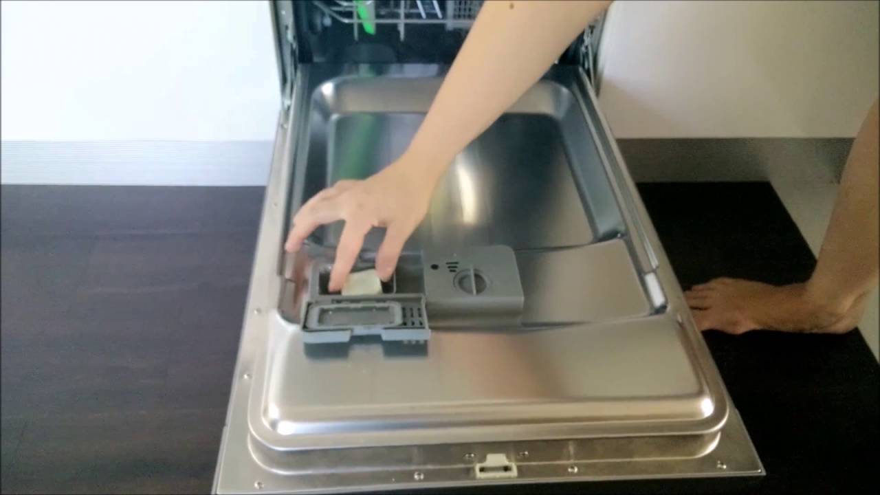 A dishwasher door showing the detergent dispenser cup and the round rinse aid reservoir cap