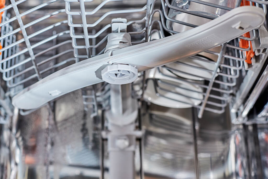 A dishwasher lower rack with a tall baking sheet positioned in front of the lower spray arm, showing how it can block rotation, real photo style