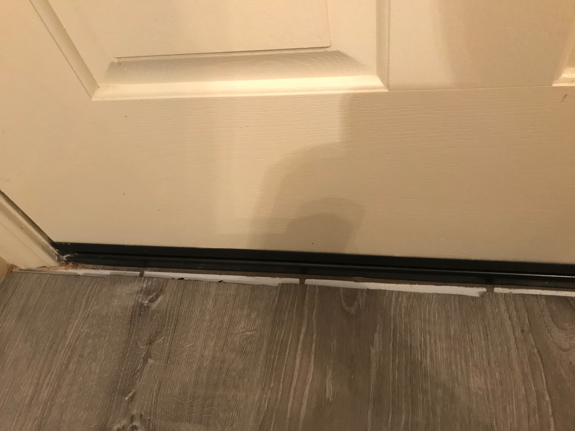 A doorway with a transition track installed on the subfloor next to newly installed vinyl plank flooring, ready for a T-molding