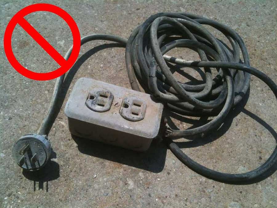 A frayed extension cord plugged into a wall outlet on a baseboard, with visible wear on the cord jacket, realistic indoor photo