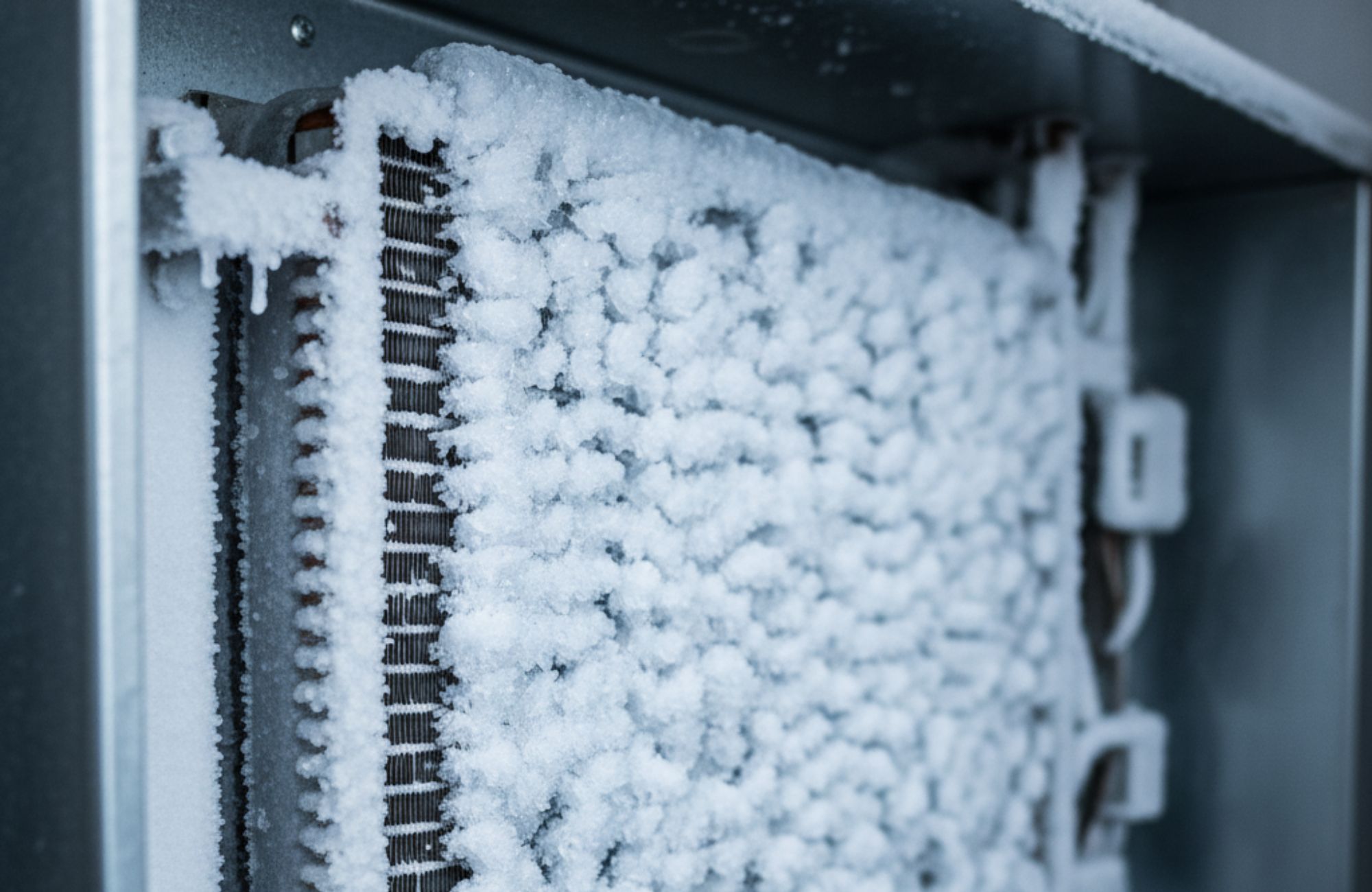 A freezer compartment with the rear panel removed showing an evaporator coil covered in thick frost buildup, realistic appliance repair photo