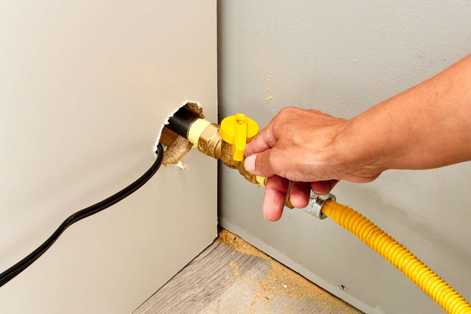 A gas shutoff valve behind a kitchen range with the lever turned perpendicular to the gas line, photographed in a real home