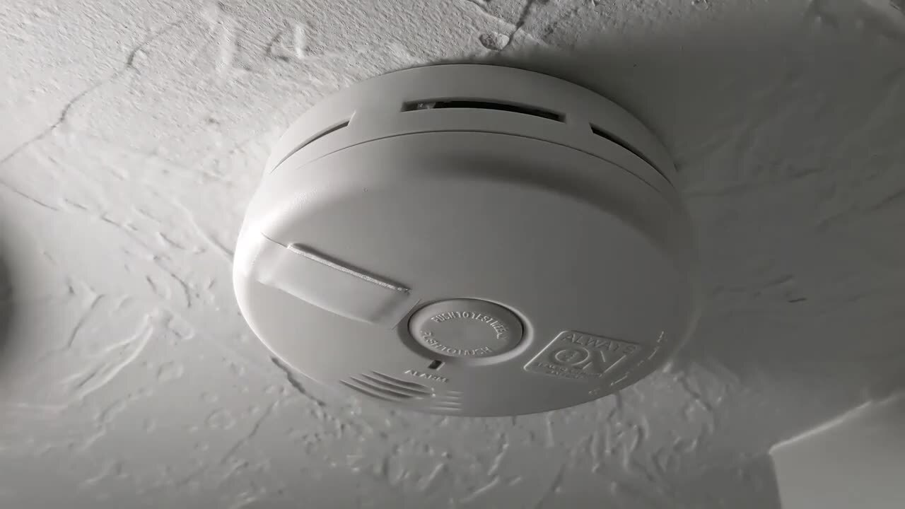 A hallway smoke alarm mounted on the ceiling near a bathroom doorway, showing a location where steam could drift toward the alarm